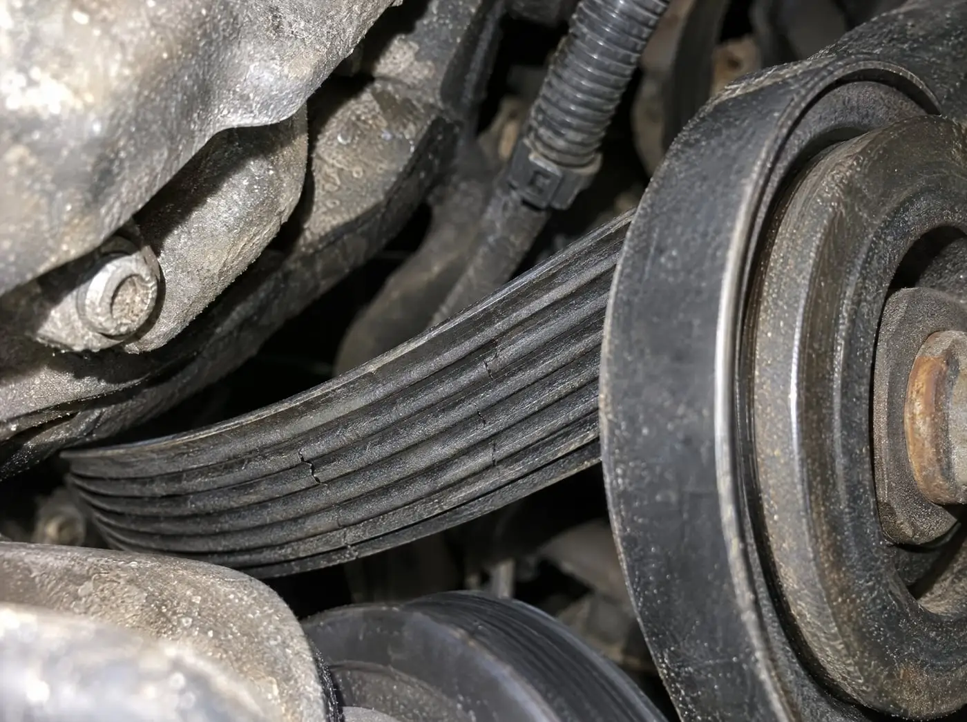 A serpentine belt on an engine pulley with a few small cracks in the ribs, lit by a flashlight
