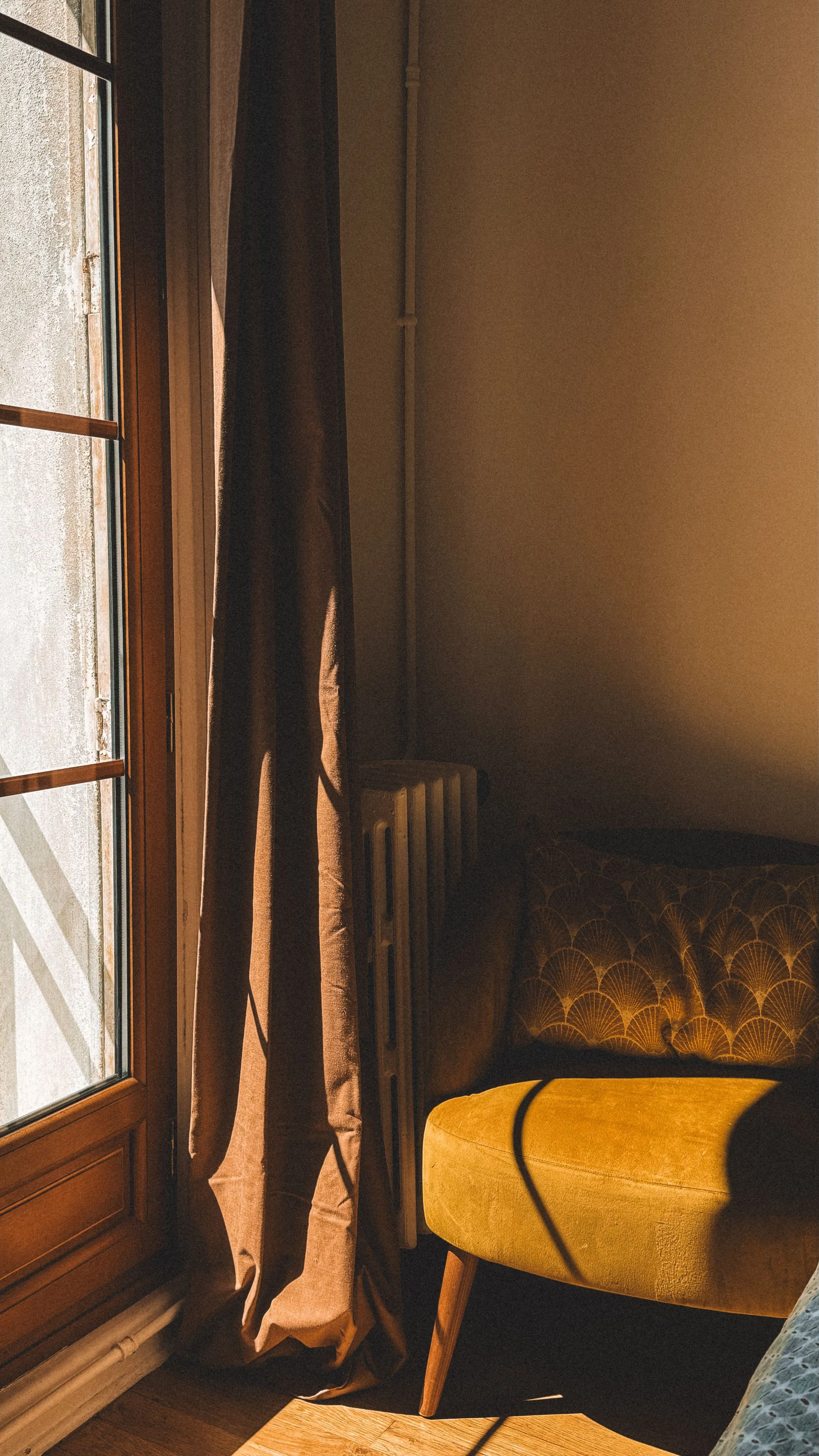 A mustard armchair in a quiet corner, lit by late sun through a tall window