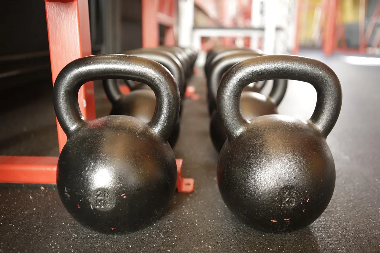 Rows of black kettlebells on a rubber floor beside a red rack