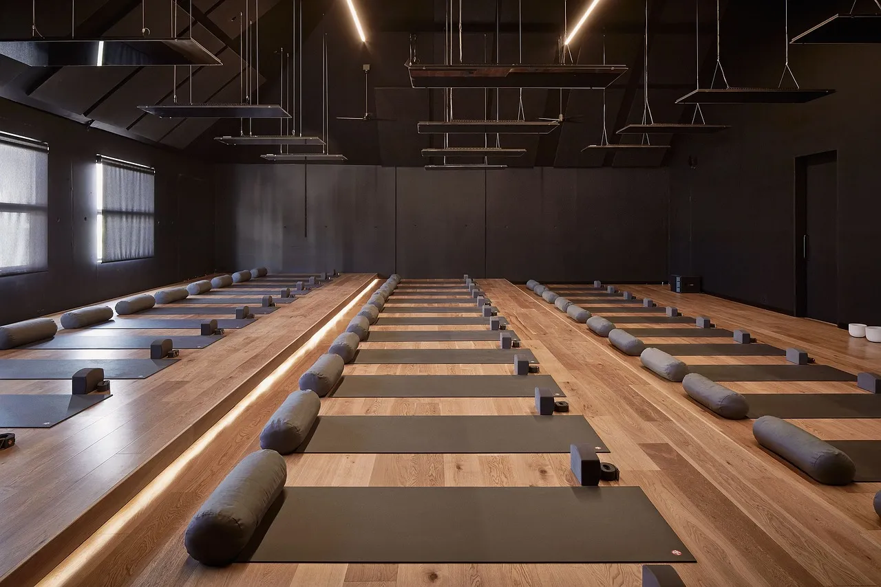 A long wood-floored class studio with mats and foam rollers laid out in rows