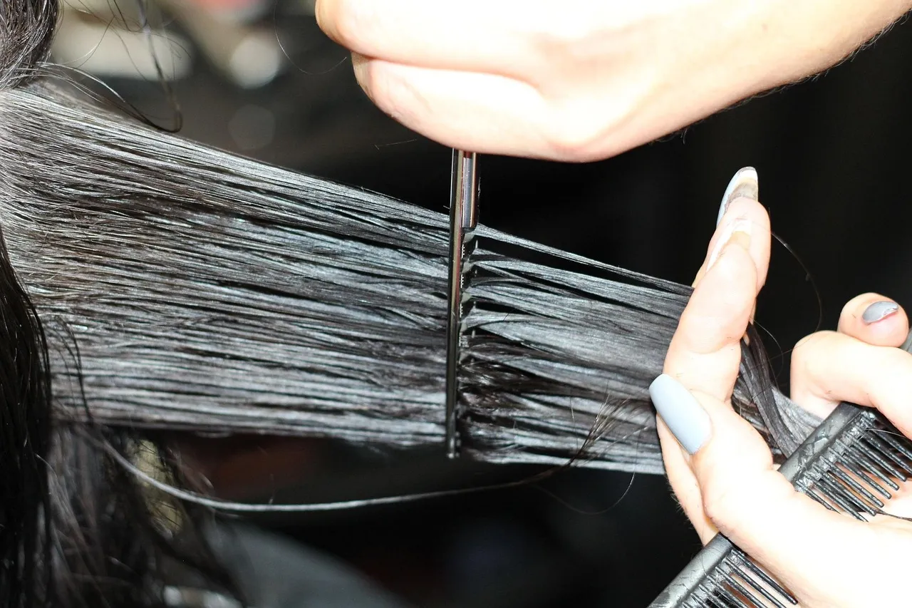 Scissors cutting a straight line through a section of dark hair