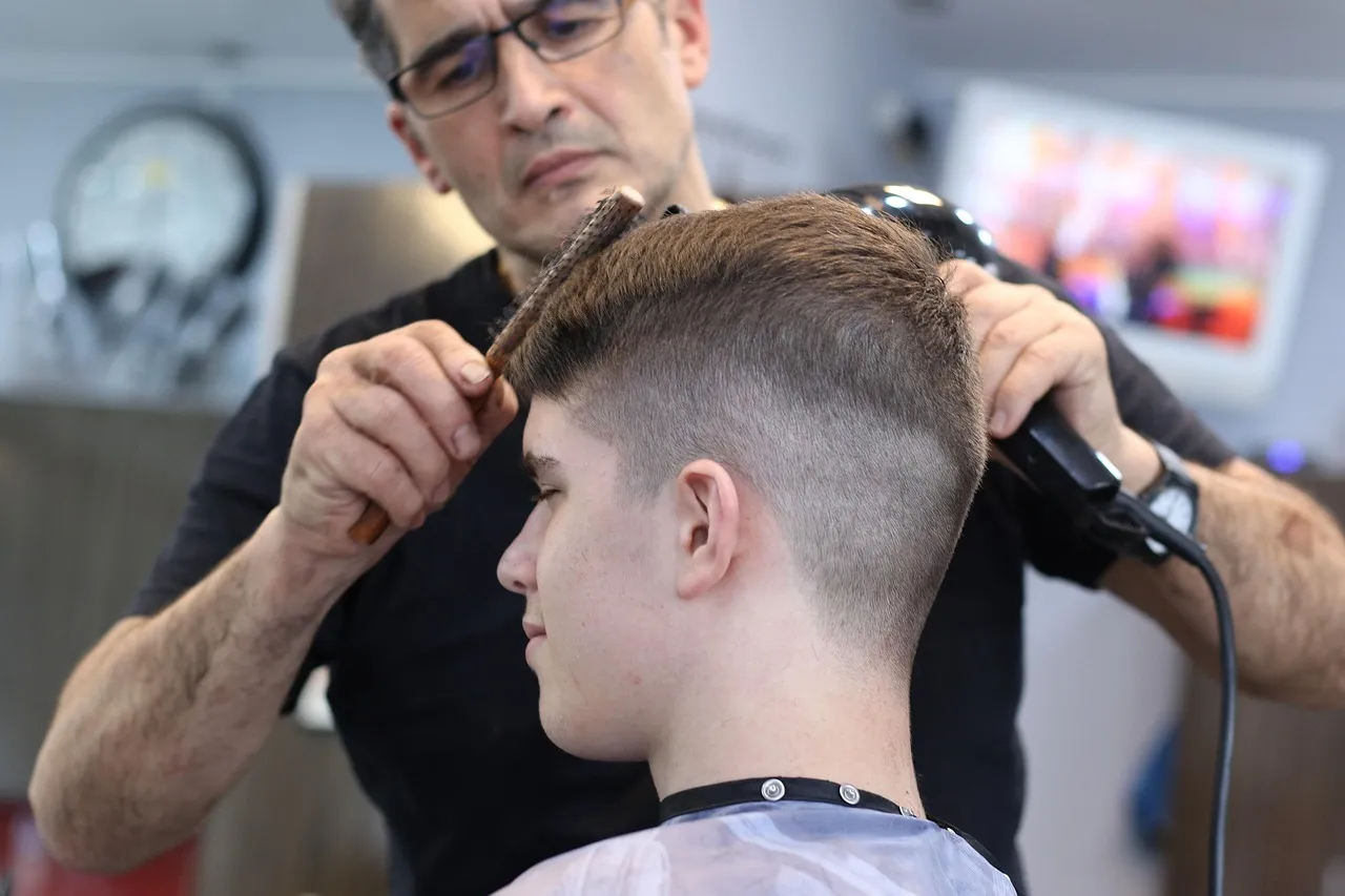 A barber blending a short fade with clippers while combing the top