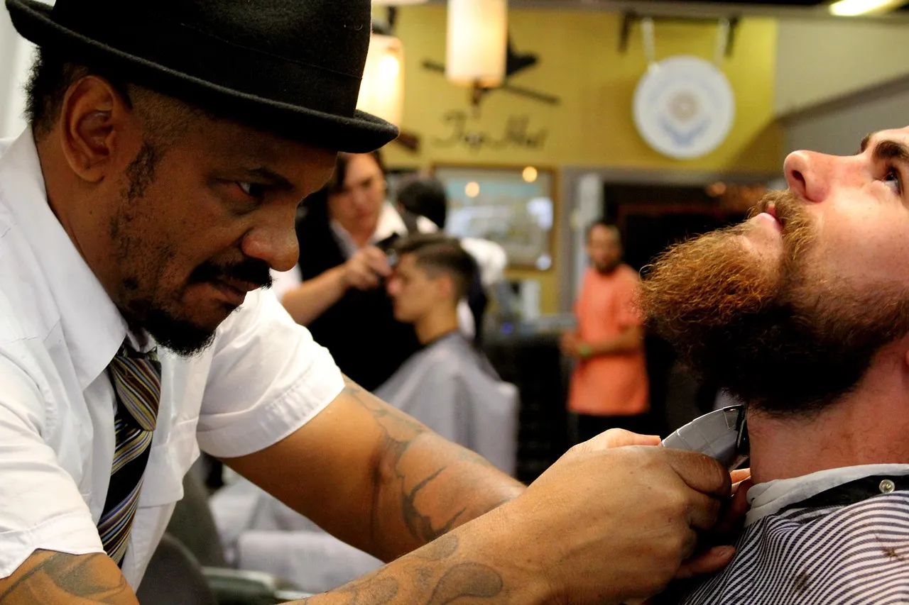 A barber lining up a full beard with a straight razor