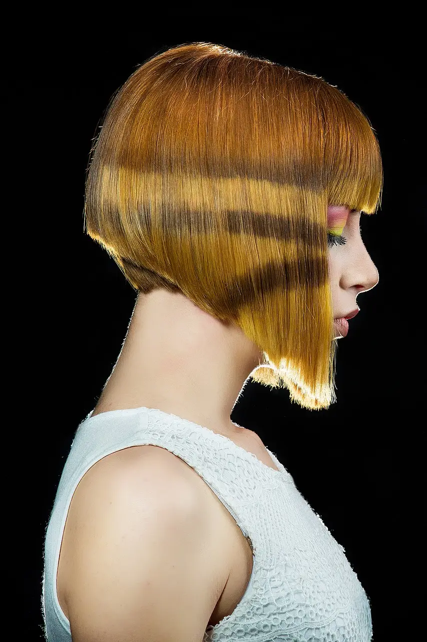 A precise bob striped in gold and brown, with a blunt fringe, in profile against black